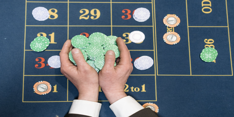 Mesa de apuestas con apuestas a varios números y manos con fichas verdes en primer plano