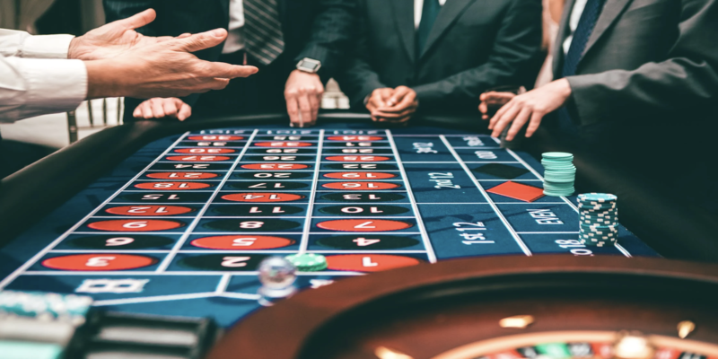 Plano de las manos de varios jugadores debatiendo y jugando a la ruleta en la mesa de juego